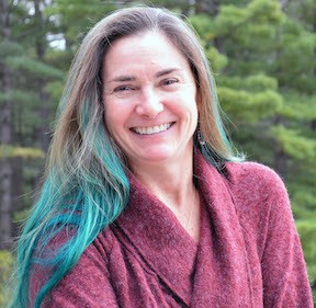white woman with ombre green hair wearing maroon sweater in front of trees
