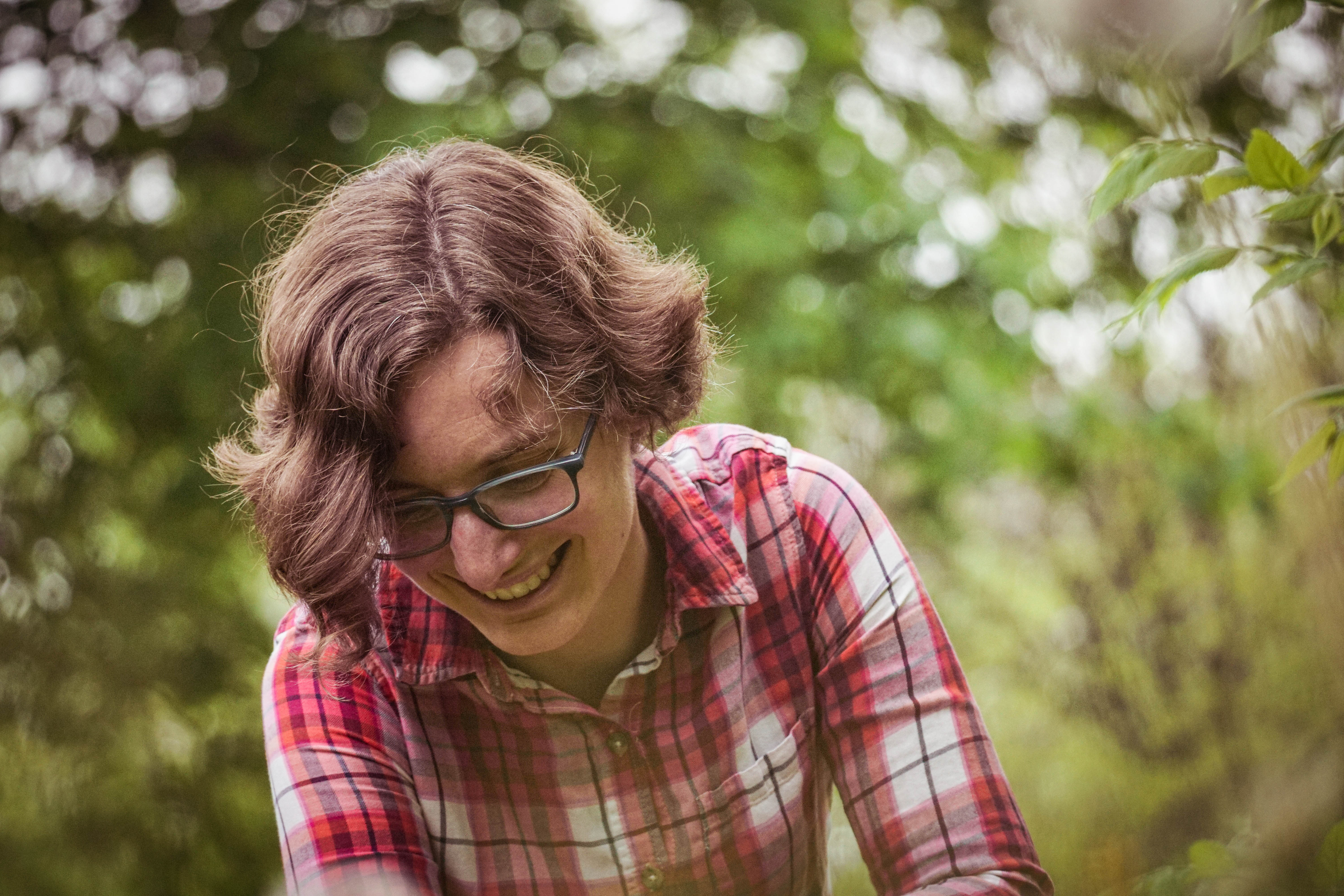 Pale skinned woman with short wavy brown hair and plaid shirt laughs while looking downward
